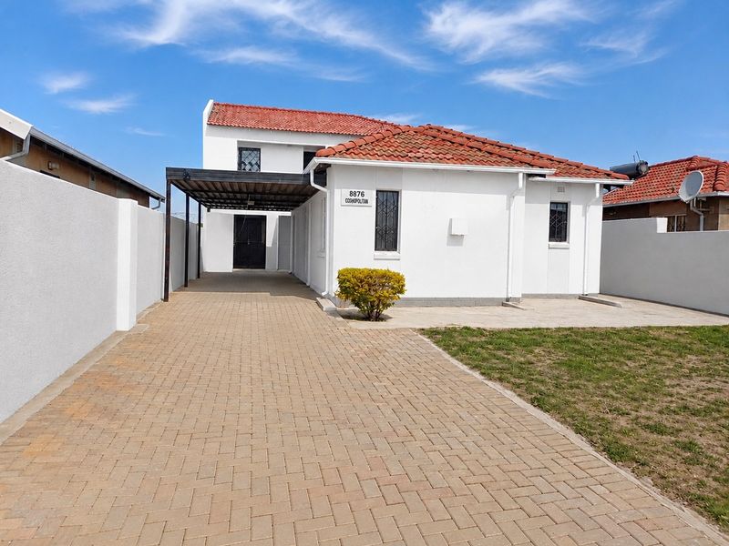 Front view of a well-maintained house featuring a paved driveway, covered carport, and secure boundary walls under a clear blue sky.