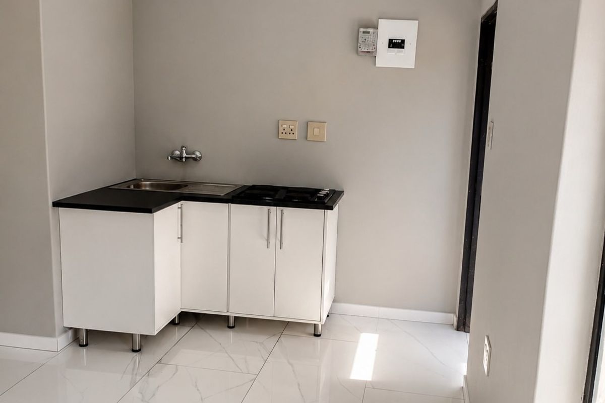 A compact, modern kitchen area featuring white cabinetry, a dark countertop with an integrated sink and hob, and polished marble-look floor tiles.