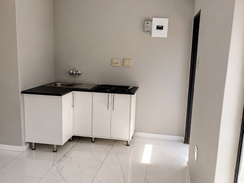 A compact, modern kitchen area featuring white cabinetry, a dark countertop with an integrated sink and hob, and polished marble-look floor tiles.