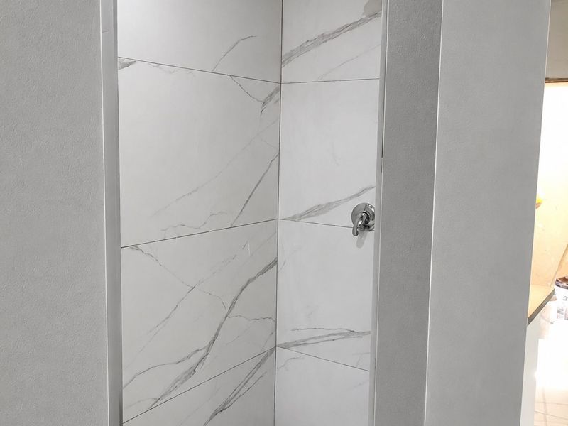 A modern, walk-in shower enclosure featuring clean marble-look porcelain tiling and contemporary chrome fixtures.