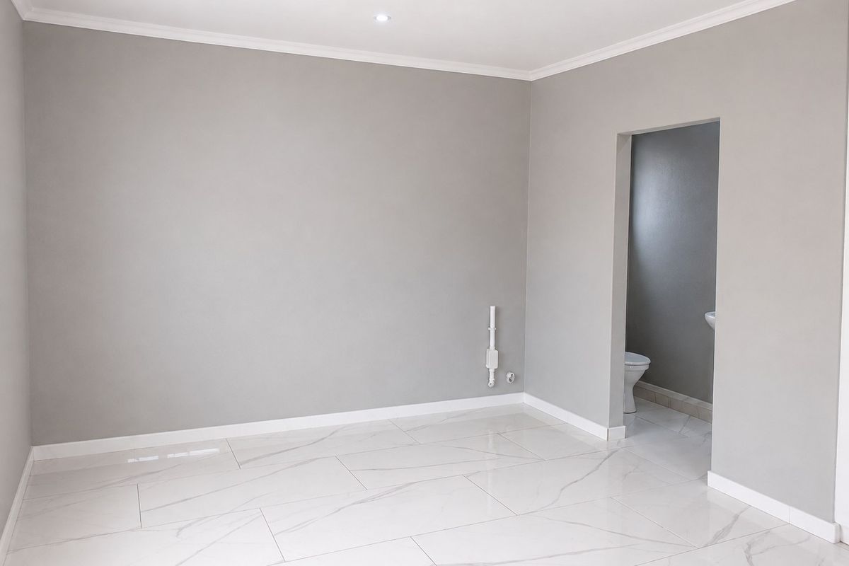 A bright, empty bedroom featuring modern marble-look floor tiles, neutral grey walls, and direct access to an en-suite bathroom.