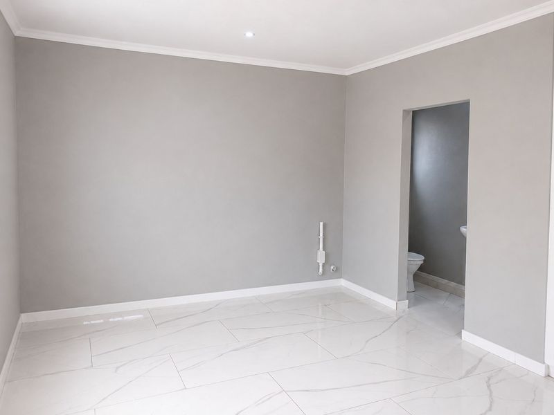 A bright, empty bedroom featuring modern marble-look floor tiles, neutral grey walls, and direct access to an en-suite bathroom.