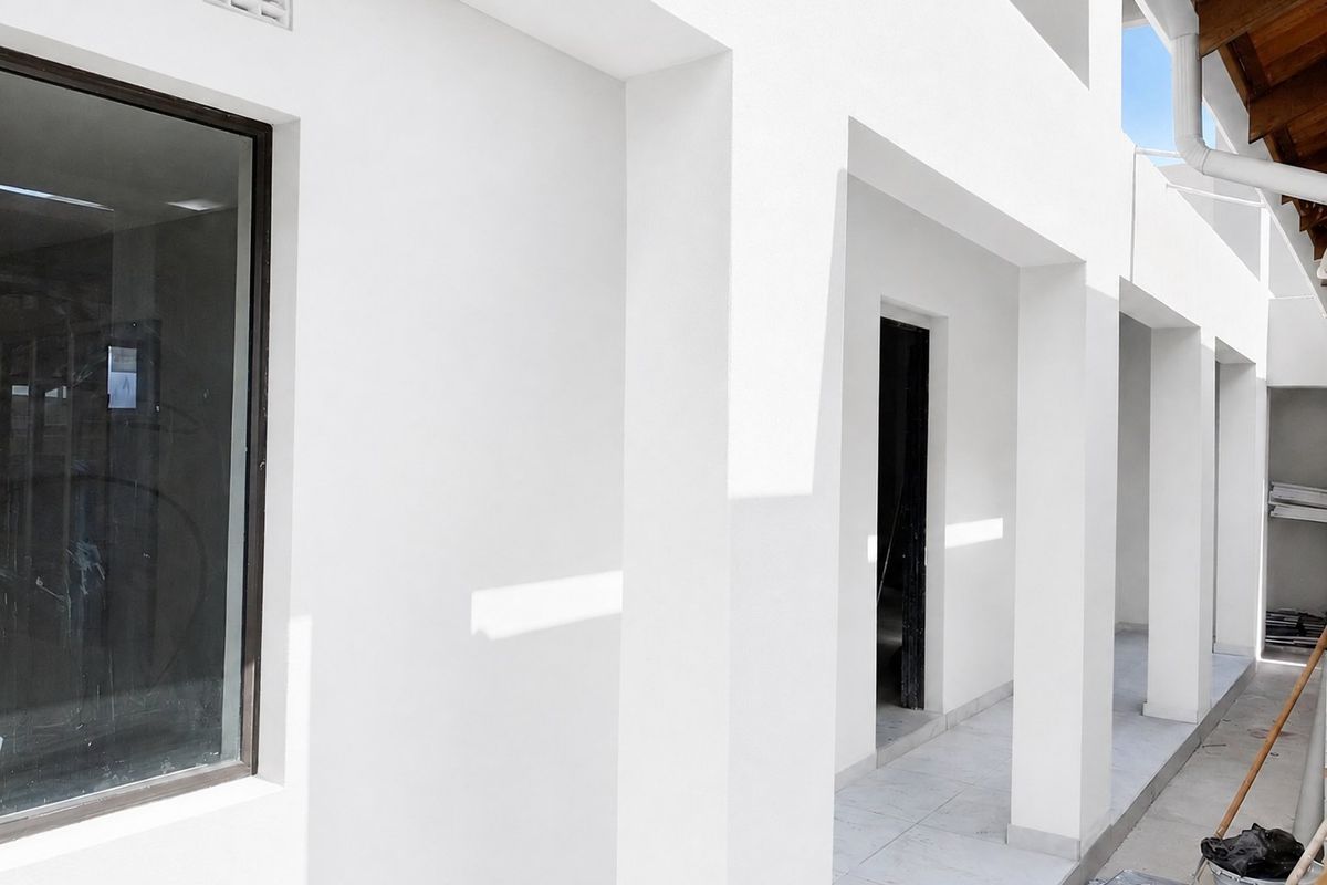 A modern covered patio area featuring clean white structural pillars, tiled flooring, and exposed timber roof detailing.
