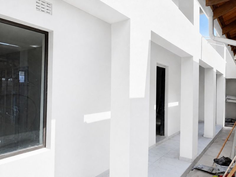 A modern covered patio area featuring clean white structural pillars, tiled flooring, and exposed timber roof detailing.