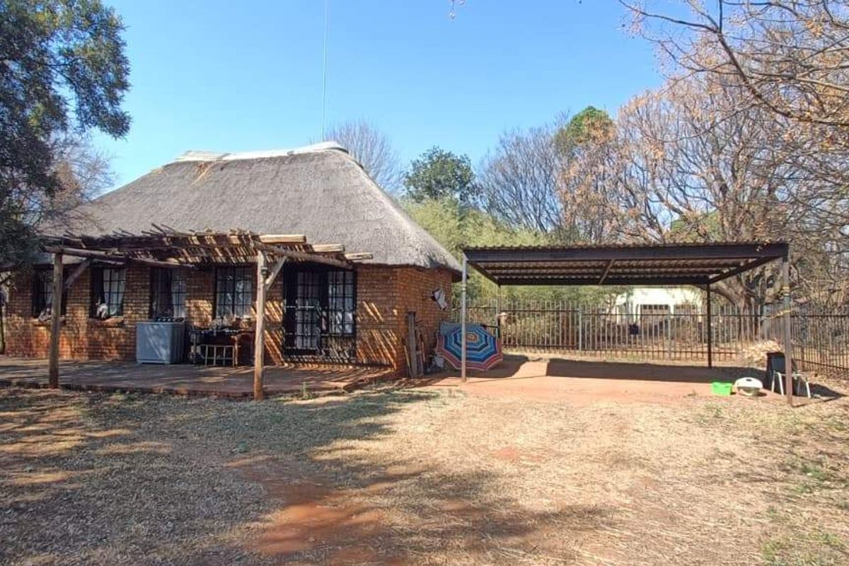 Rear view of a rustic brick farmhouse featuring a traditional thatch roof, a covered patio area, and an adjacent metal carport structure.