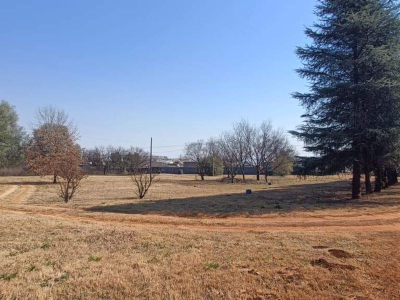 Expansive open farm land featuring mature trees and a dirt access road, offering a natural and spacious outdoor setting.