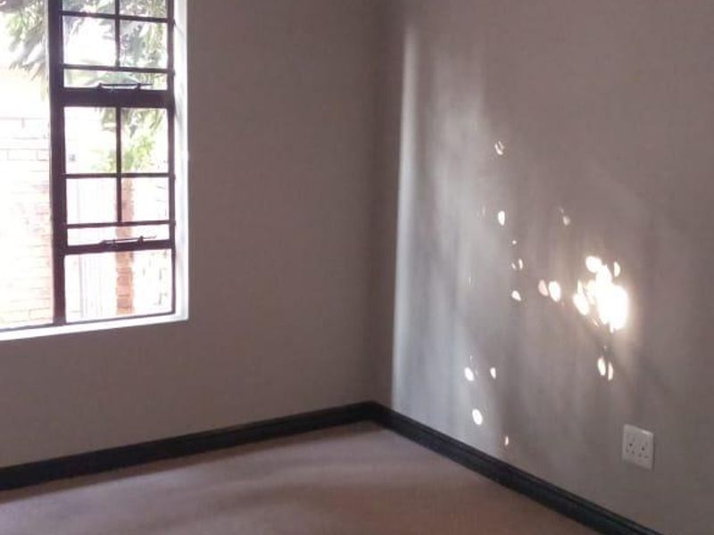 A clean, empty bedroom featuring neutral wall paint, carpeted flooring, and a window with a metal frame.