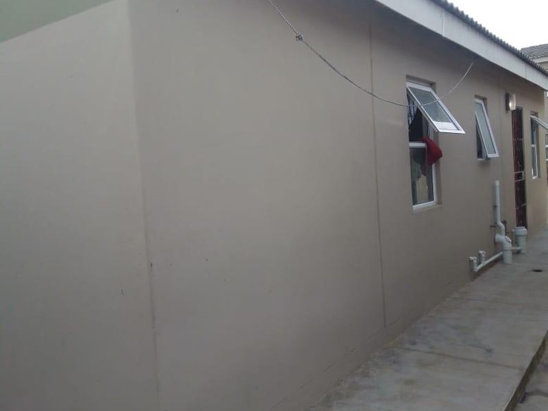 A view of the rear exterior elevation featuring a concrete walkway, external plumbing, and casement windows along the side of the house.