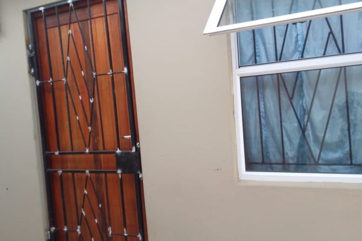 Exterior view of a rear wall featuring a timber door with a security gate and a top-hung window with security bars.