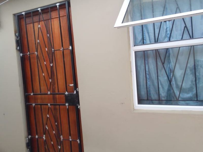 Exterior view of a rear wall featuring a timber door with a security gate and a top-hung window with security bars.