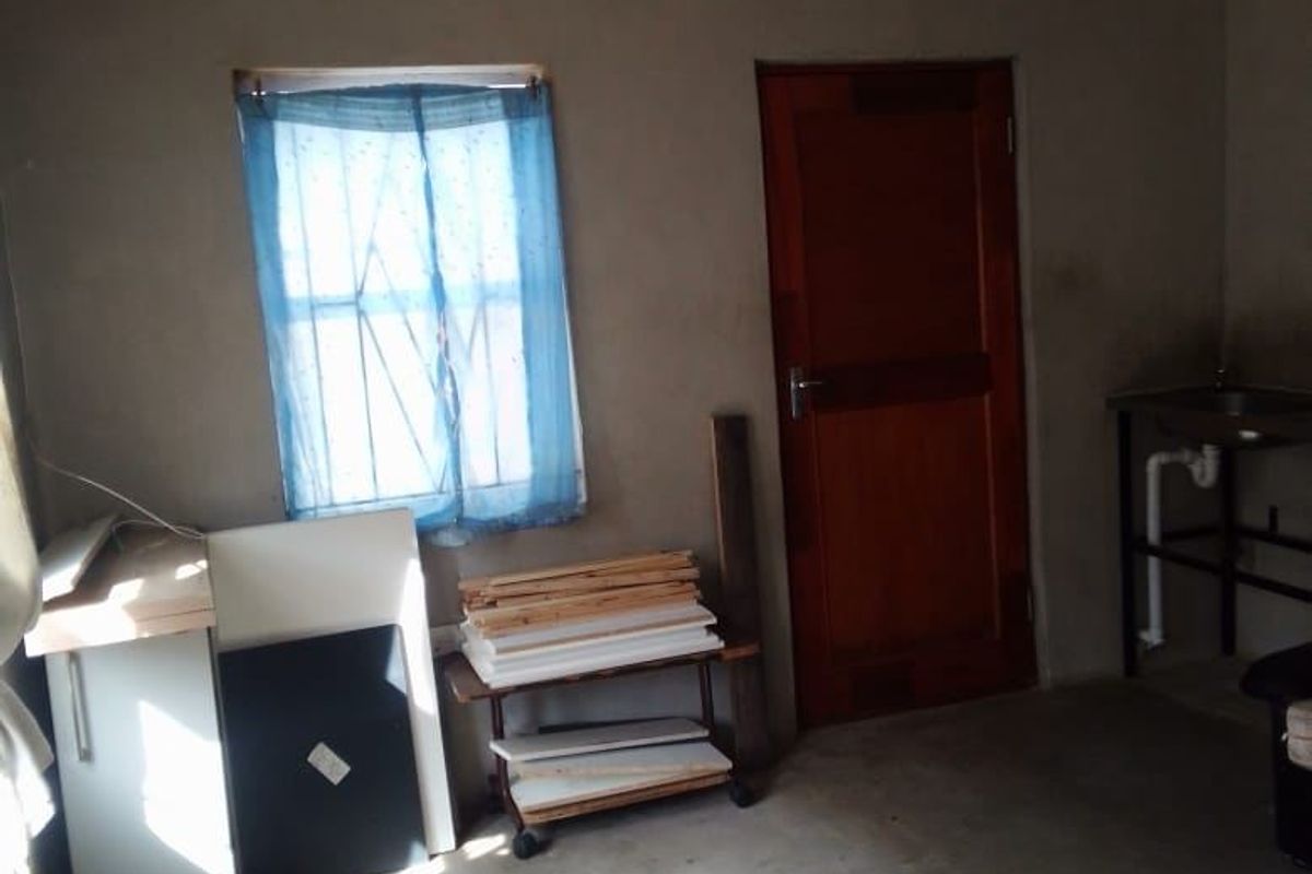 A basic utility or storage space featuring concrete flooring, a timber door, and a window with security bars, requiring cosmetic updates.