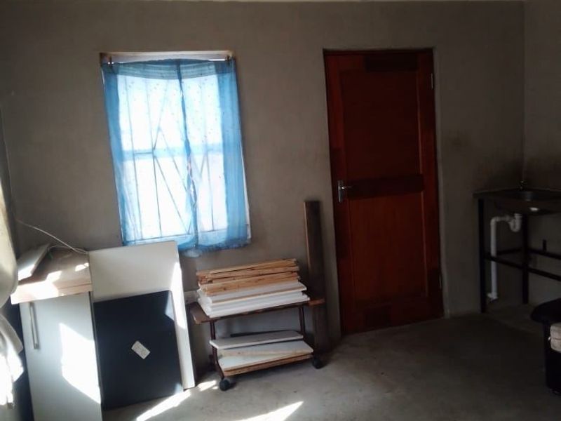 A basic utility or storage space featuring concrete flooring, a timber door, and a window with security bars, requiring cosmetic updates.