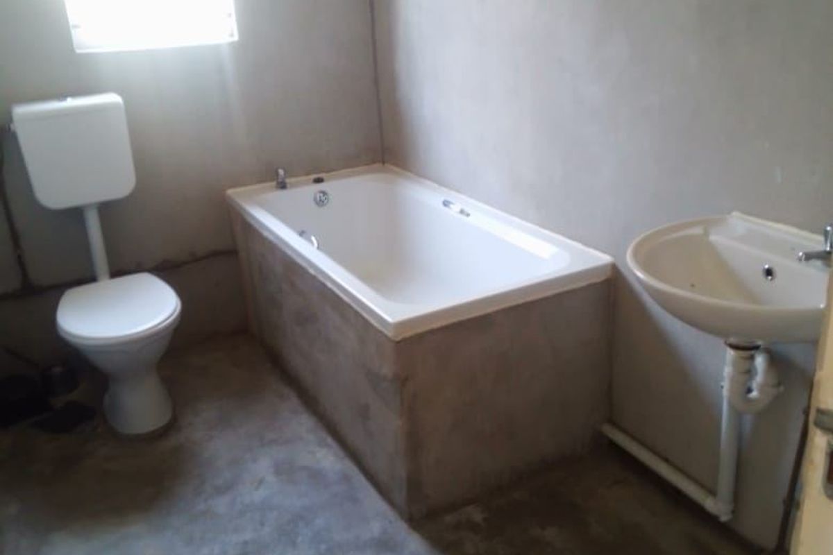 An unfinished bathroom featuring a bathtub, toilet, and pedestal basin with exposed cement floors and unpainted plaster walls, requiring final finishes.