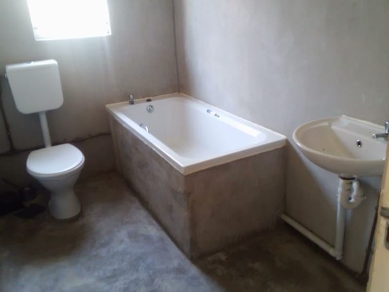 An unfinished bathroom featuring a bathtub, toilet, and pedestal basin with exposed cement floors and unpainted plaster walls, requiring final finishes.