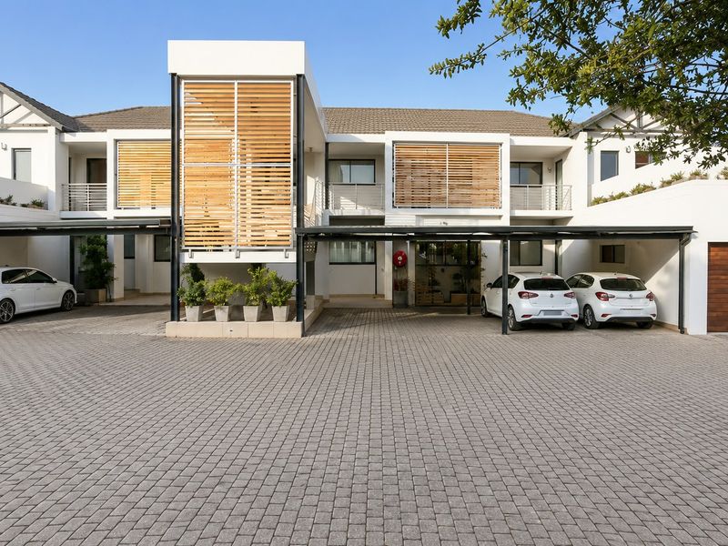 Modern cluster home exterior featuring a paved driveway, integrated carports, timber privacy screens, and a secure garage entrance.