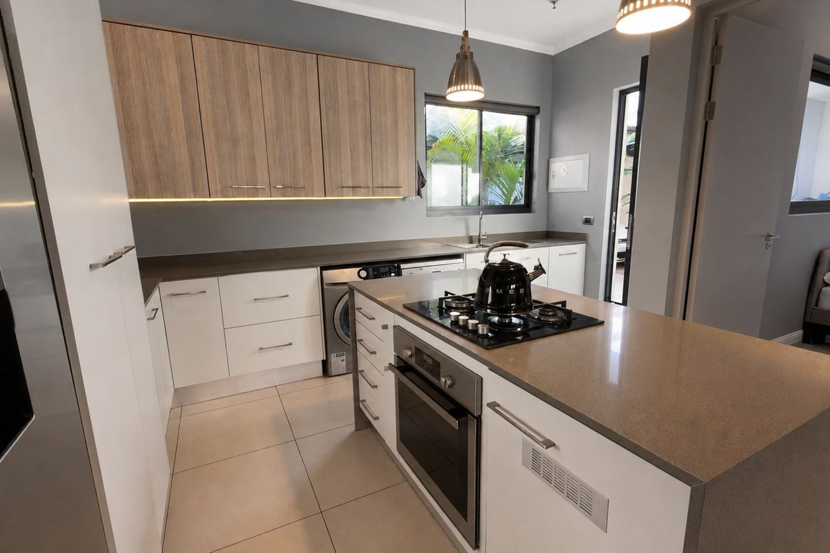 Modern kitchen featuring a central island with a gas hob and oven, stone countertops, two-tone cabinetry, and integrated laundry appliance space.