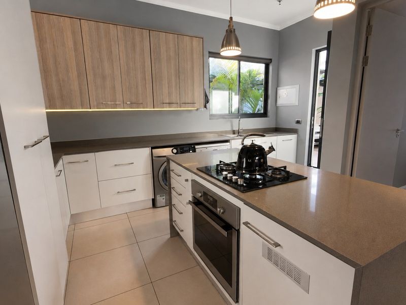 Modern kitchen featuring a central island with a gas hob and oven, stone countertops, two-tone cabinetry, and integrated laundry appliance space.