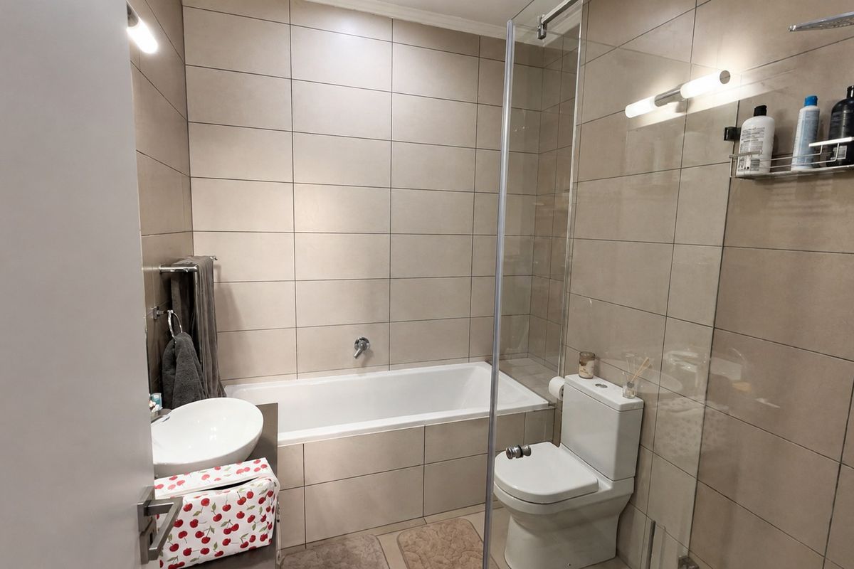 Modern bathroom featuring a built-in bathtub, glass shower screen, wall-mounted basin, and toilet with neutral floor-to-ceiling wall tiling.