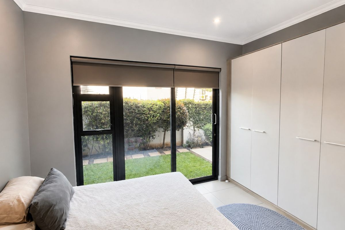 A modern bedroom featuring built-in cupboards, tiled flooring, and a large sliding glass door providing direct access to the garden.