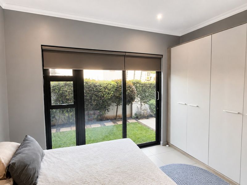 A modern bedroom featuring built-in cupboards, tiled flooring, and a large sliding glass door providing direct access to the garden.