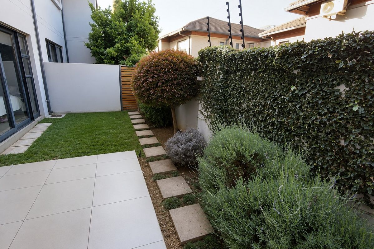 A well-maintained rear garden featuring a tiled patio, manicured lawn, stone pathway, and established greenery against a secure boundary wall.