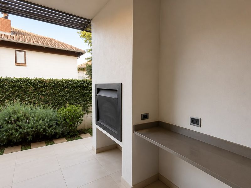 A clean, covered patio area featuring a built-in braai, stone prep counter, and tiled flooring, overlooking a private garden space.