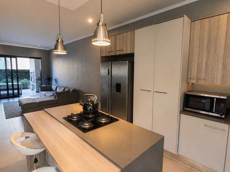 Modern open-plan living area featuring a contemporary kitchen with a central island, gas hob, stone countertops, and seamless flow to the outdoor patio.