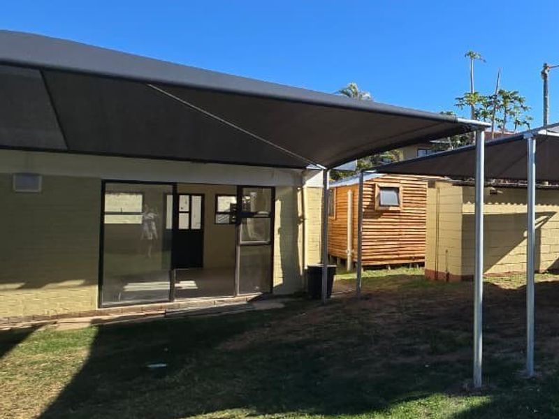 Rear exterior view of the property featuring a large shade sail, sliding glass doors, and a small backyard area.