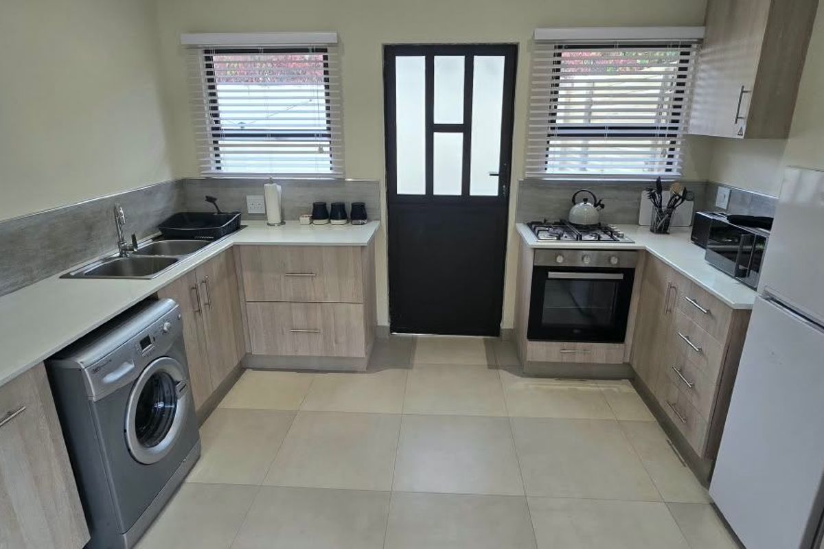 Modern kitchen featuring light wood-finish cabinetry, laminate countertops, built-in oven with gas hob, and tiled flooring with direct exterior access.