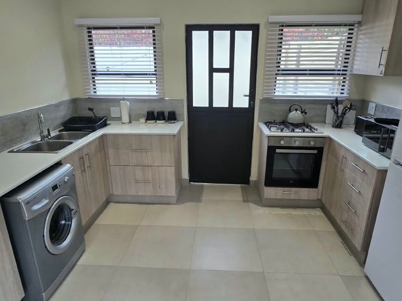 Modern kitchen featuring light wood-finish cabinetry, laminate countertops, built-in oven with gas hob, and tiled flooring with direct exterior access.