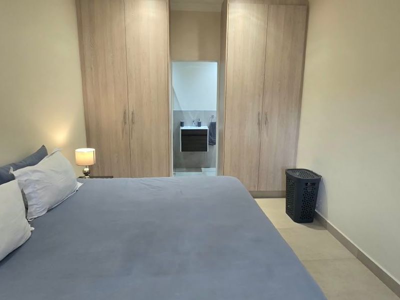 A well-maintained bedroom featuring built-in wooden cupboards, neutral tiled flooring, and direct access to an en-suite bathroom.