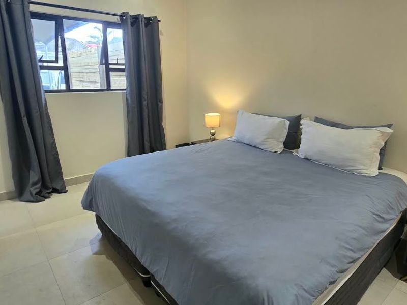 A well-maintained bedroom featuring neutral tiled flooring, a sliding window, and clean wall finishes.
