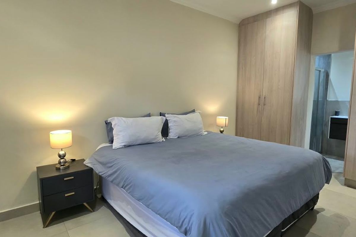 A well-maintained bedroom featuring neutral walls, tiled flooring, and ample built-in cupboard storage, with an adjoining en-suite bathroom visible.