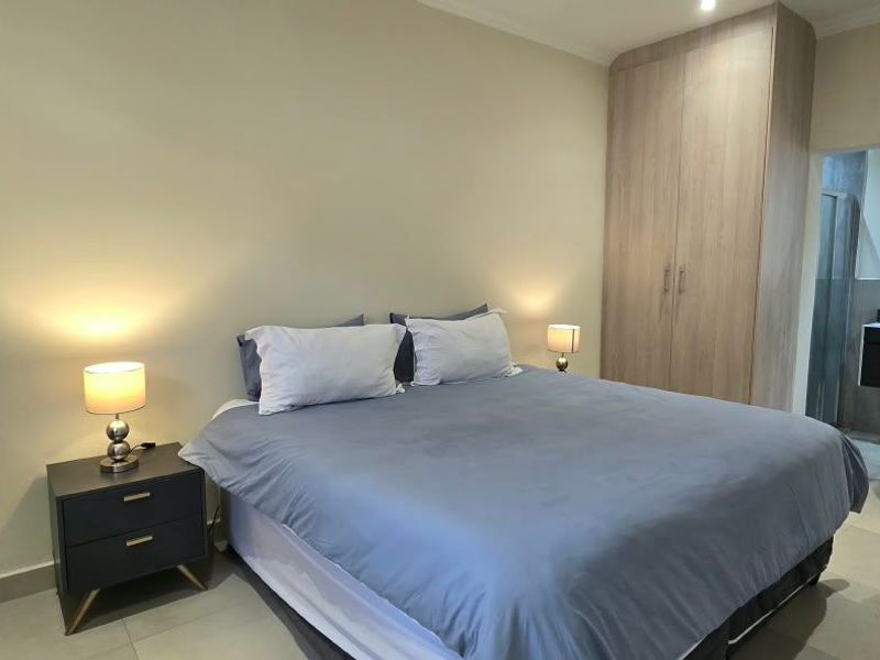 A well-maintained bedroom featuring neutral walls, tiled flooring, and ample built-in cupboard storage, with an adjoining en-suite bathroom visible.