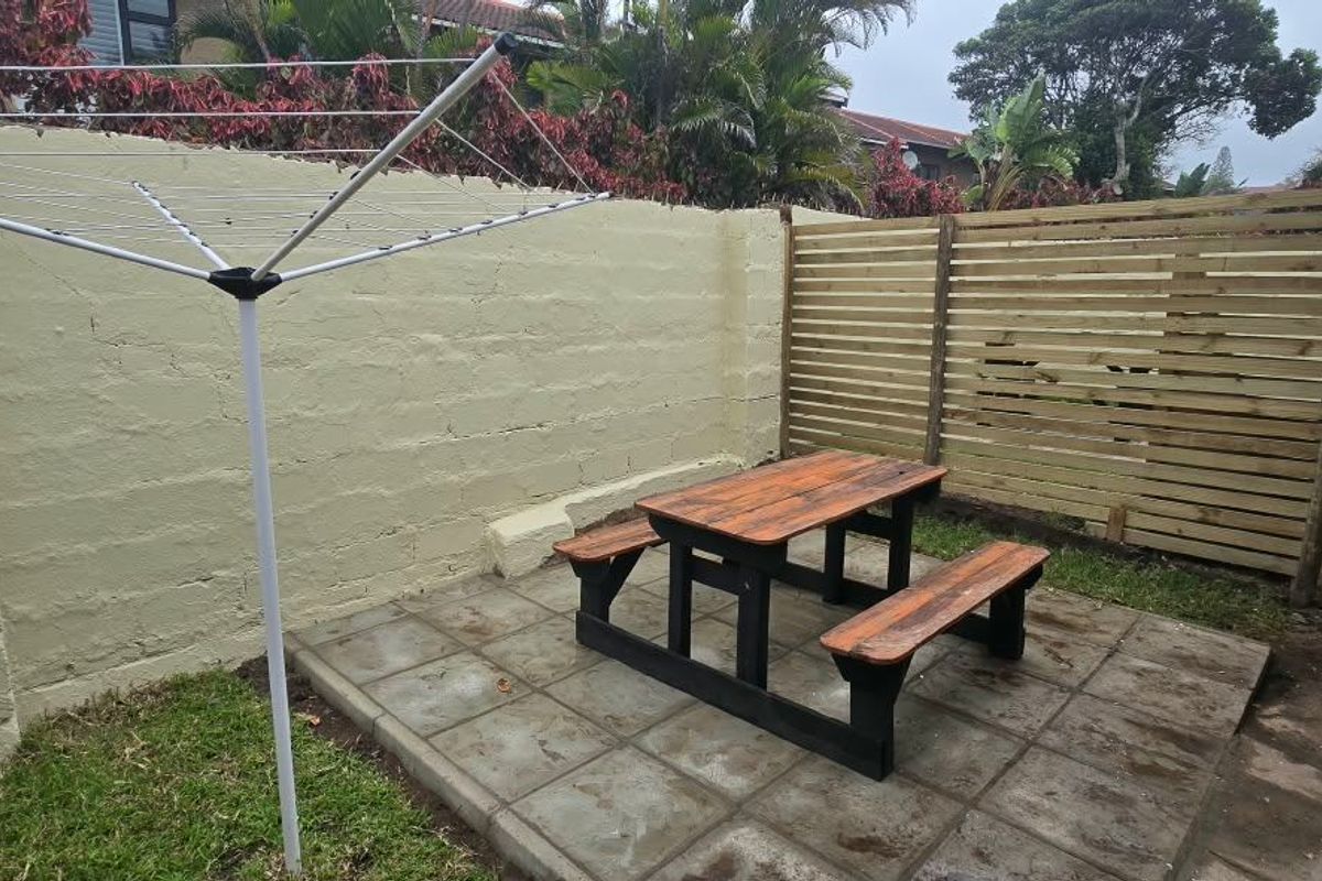 A private rear courtyard featuring a paved patio area, timber privacy screening, and a concrete block boundary wall.