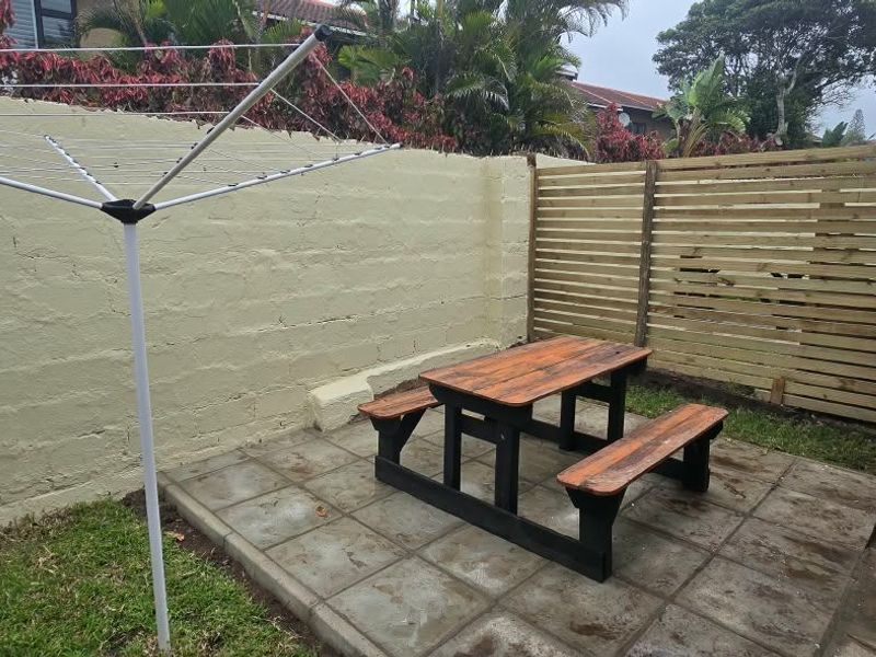 A private rear courtyard featuring a paved patio area, timber privacy screening, and a concrete block boundary wall.
