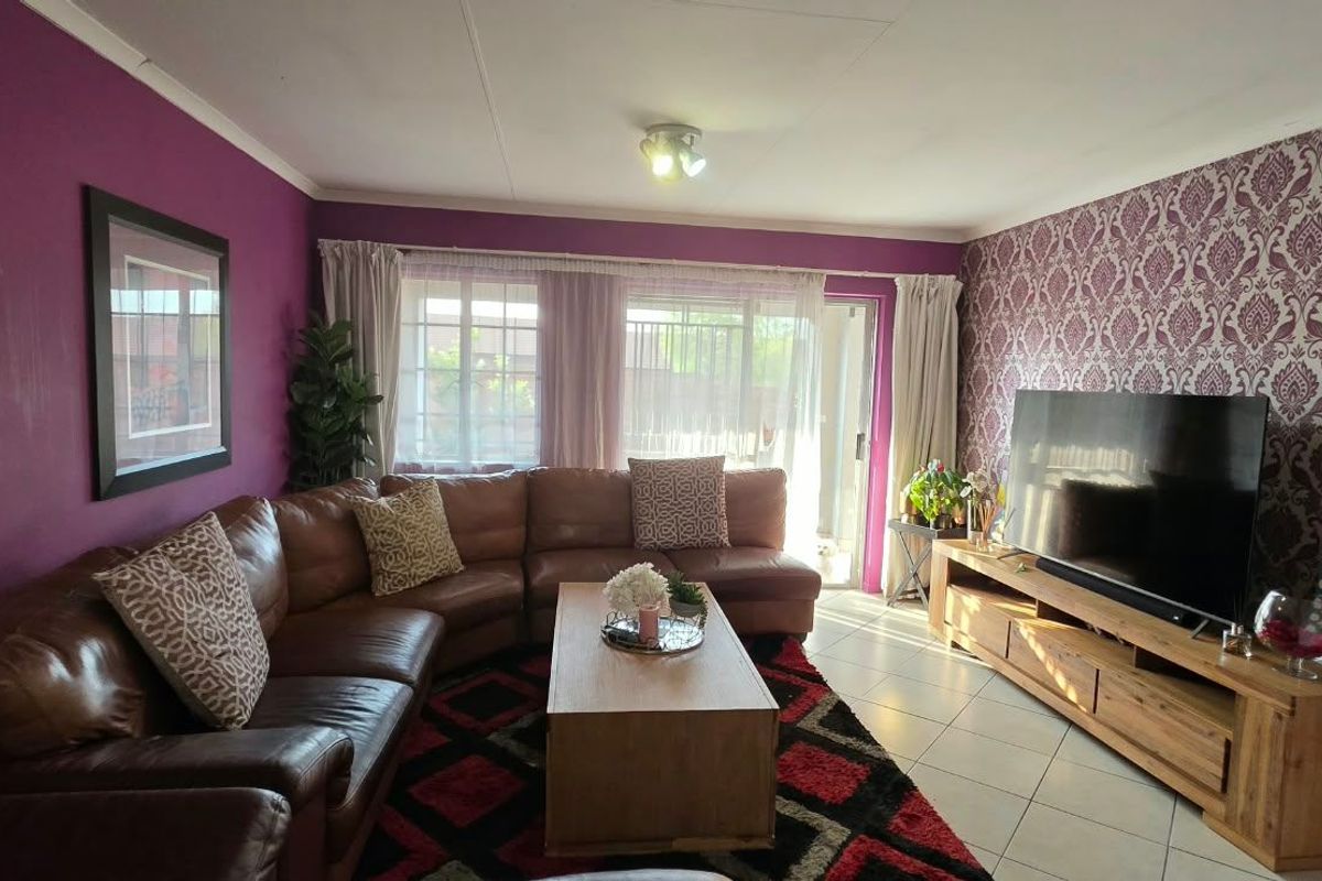 A comfortable living room featuring tiled flooring, a sliding glass door providing natural light, and a distinct accent wall.