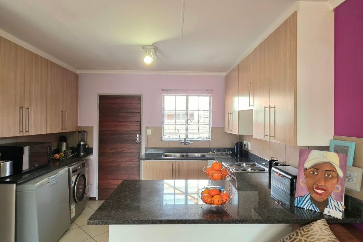 Functional kitchen featuring light wood-tone cabinetry, granite countertops, a double bowl sink, and an electric hob, with tiled flooring throughout.