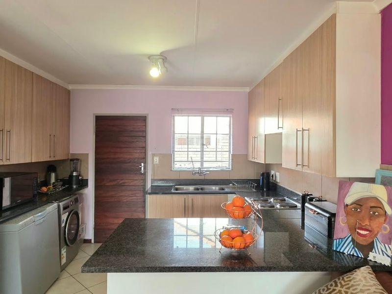 Functional kitchen featuring light wood-tone cabinetry, granite countertops, a double bowl sink, and an electric hob, with tiled flooring throughout.