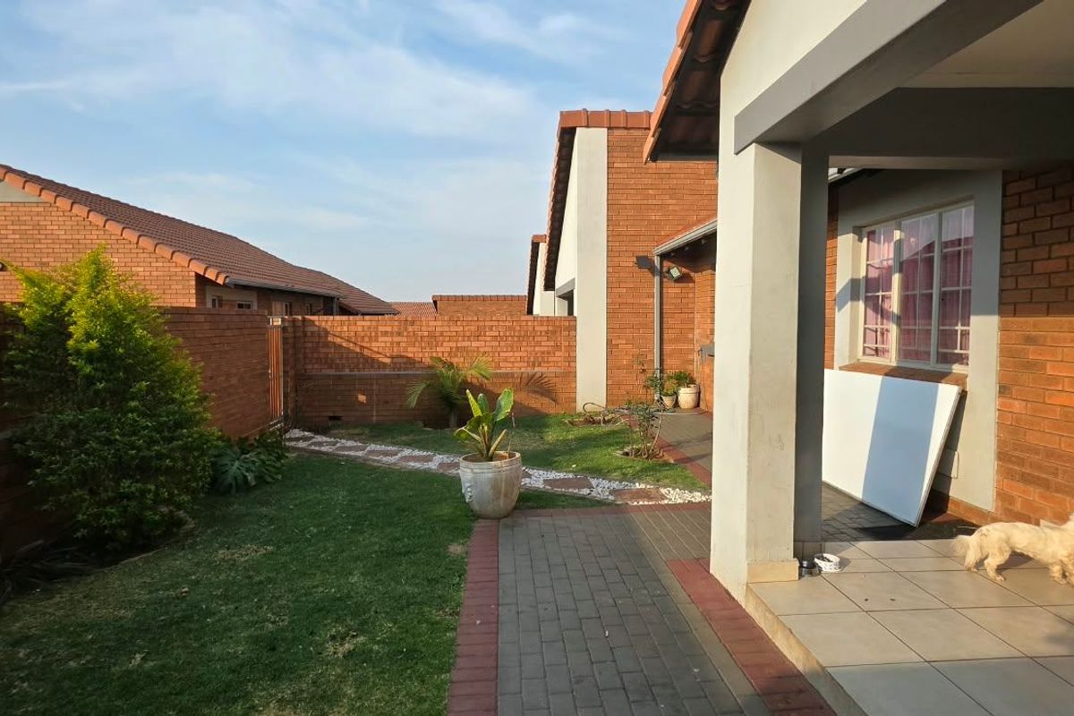 A private rear garden featuring a paved walkway, a covered patio area, and brick boundary walls, providing a low-maintenance outdoor space.