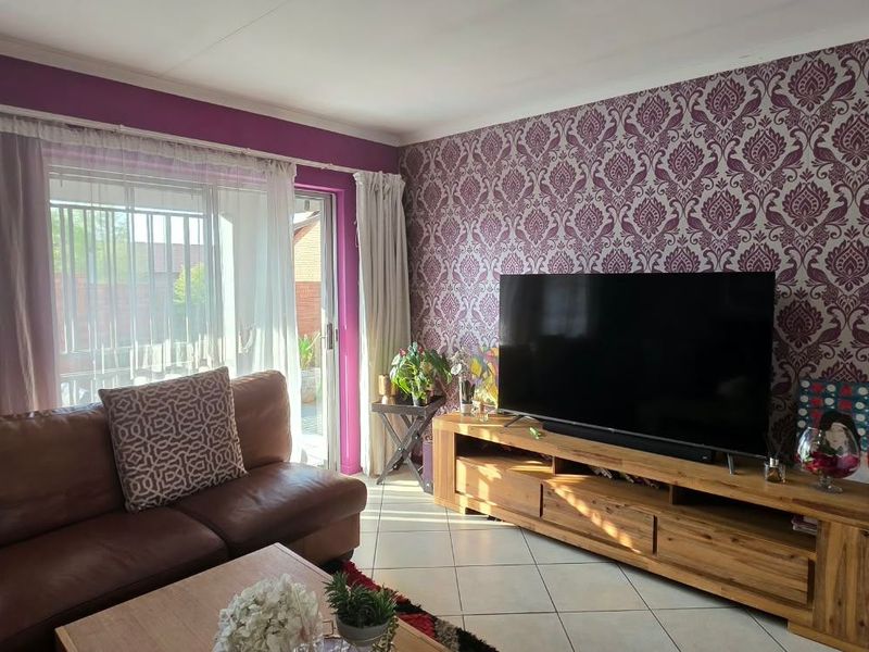 A living room featuring tiled flooring, a large sliding glass door providing natural light, and a decorative feature wall.