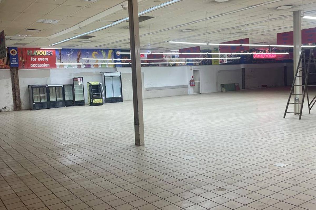 Spacious open-plan commercial retail area featuring tiled flooring, suspended ceilings with integrated lighting, and structural support columns.