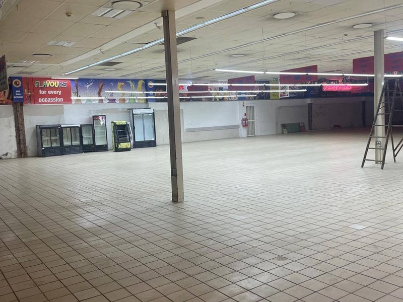Spacious open-plan commercial retail area featuring tiled flooring, suspended ceilings with integrated lighting, and structural support columns.