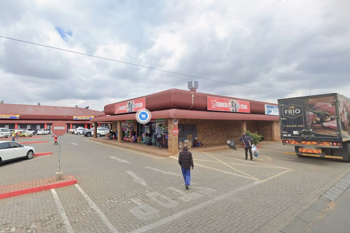 Exterior view of a commercial retail strip center featuring a brick facade, covered walkways, and an expansive paved parking area.