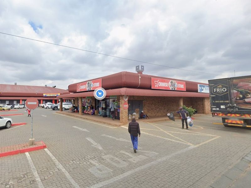 Exterior view of a commercial retail strip center featuring a brick facade, covered walkways, and an expansive paved parking area.