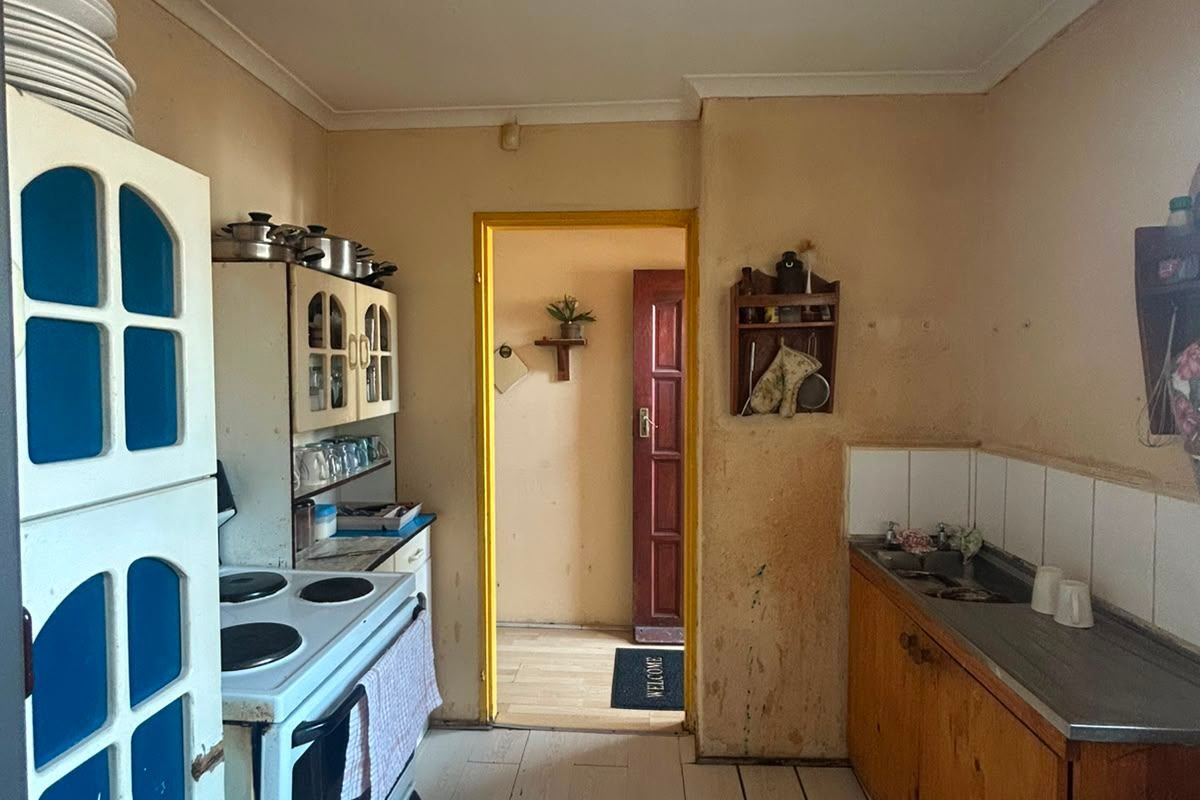 A dated kitchen featuring original cabinetry, a stainless steel sink, and a freestanding stove, requiring significant cosmetic updates and refurbishment.