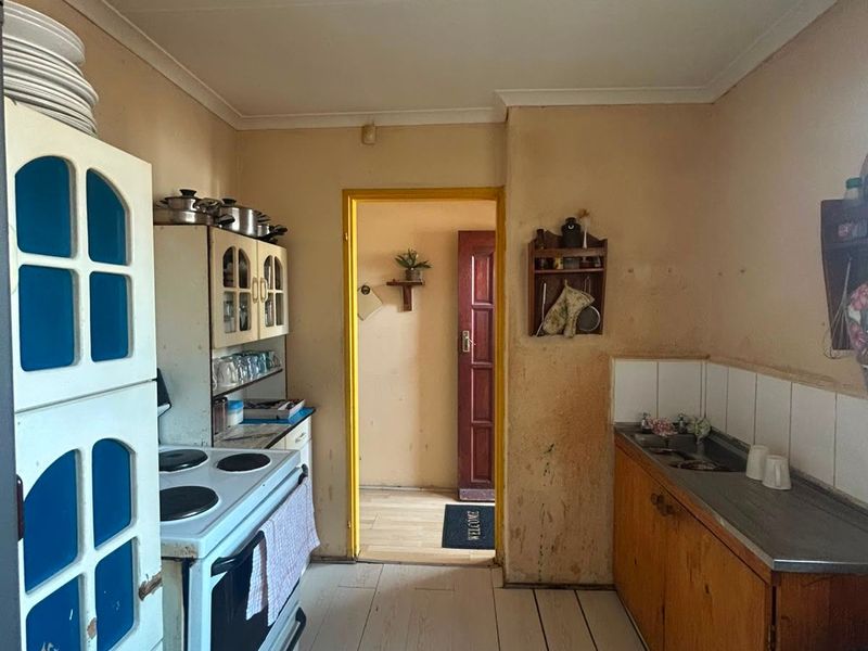 A dated kitchen featuring original cabinetry, a stainless steel sink, and a freestanding stove, requiring significant cosmetic updates and refurbishment.