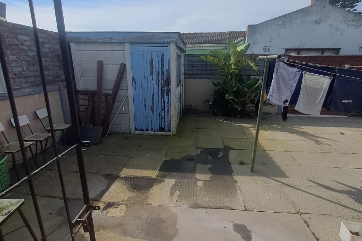 A rear courtyard area featuring paved flooring, a boundary wall, and a small outbuilding with a weathered door.