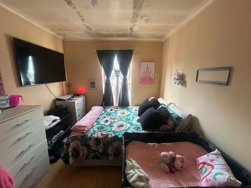 A bedroom featuring laminate flooring and a window, currently showing significant signs of ceiling water damage and deterioration requiring repair.