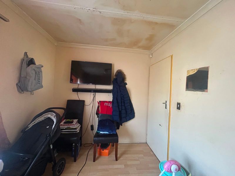 A bedroom space featuring laminate flooring, currently showing significant ceiling water damage and wall surface deterioration requiring maintenance and repair.